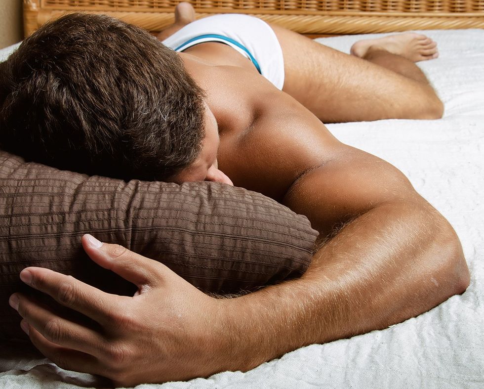 low angle man in underwear laying on his stomach in bed head on pillow body stretched out