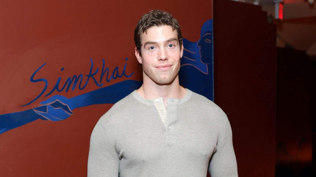 Man in beige sweater stands in front of a mural