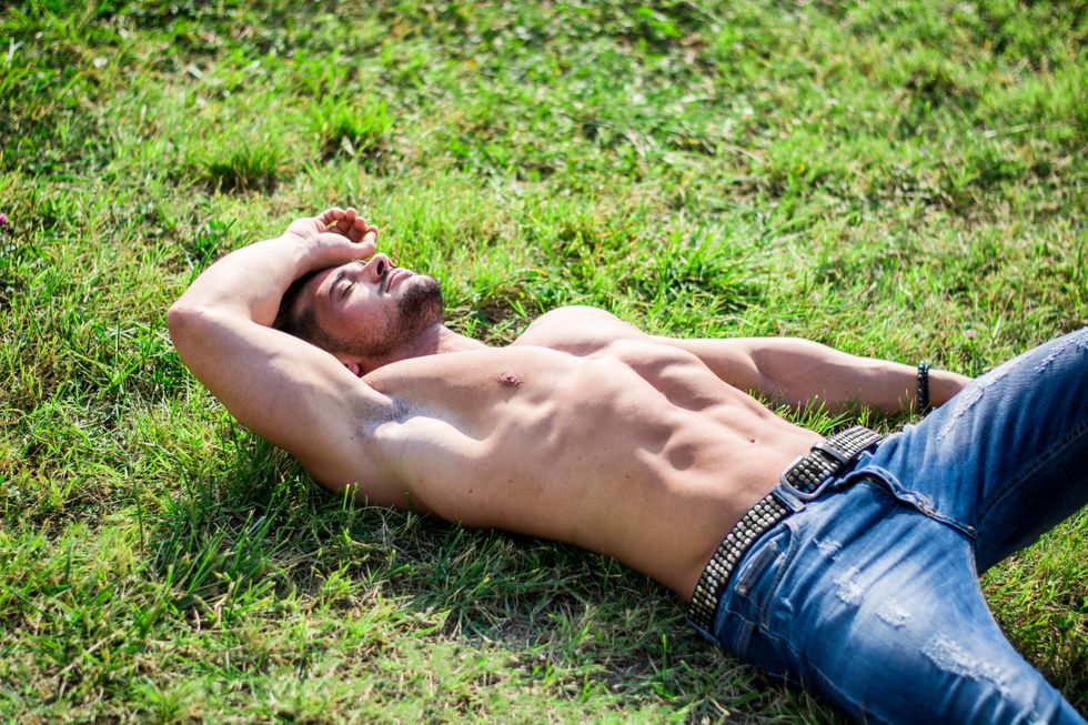 man in jeans with studded belt no shirt sun bathing on the grass