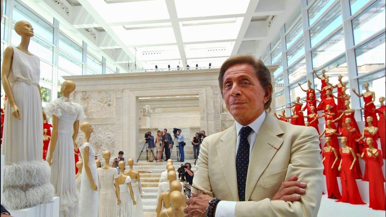 Man in suit stands among mannequins in elegant dresses in a bright, spacious showroom.