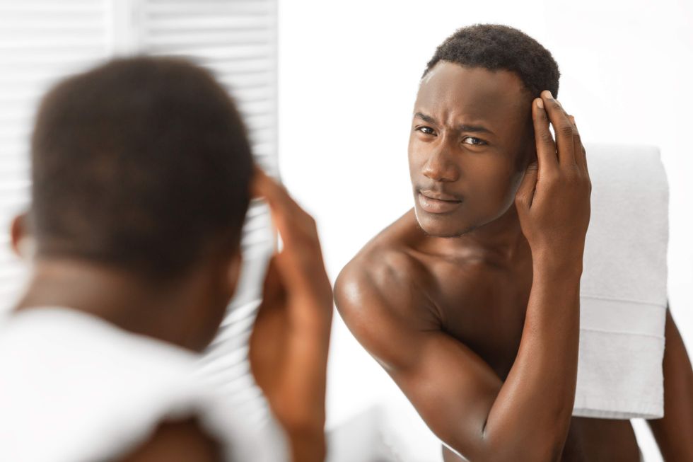 Man looking in the mirror at his hairline.