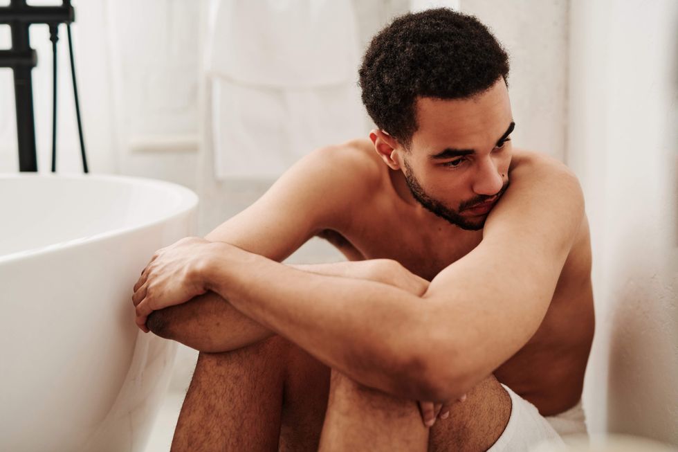 Man looking sad, sitting on the floor of a bathroom