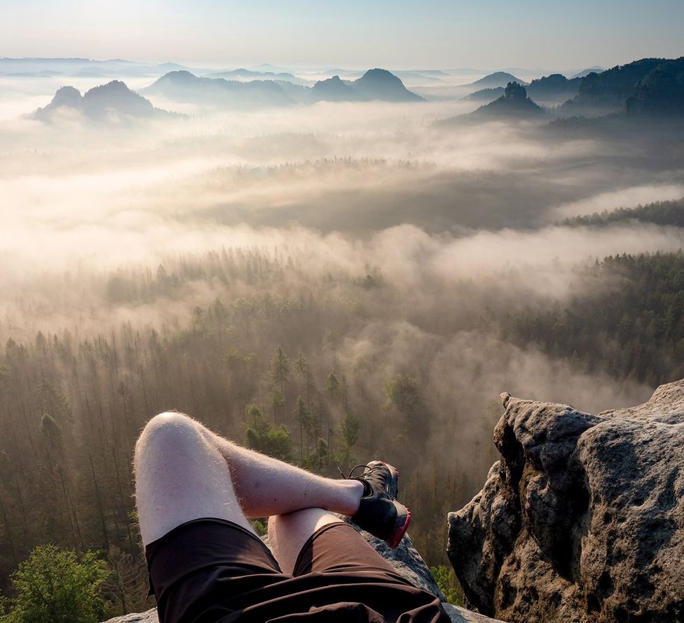 man on hike relaxing on cliff edge with forest mist below