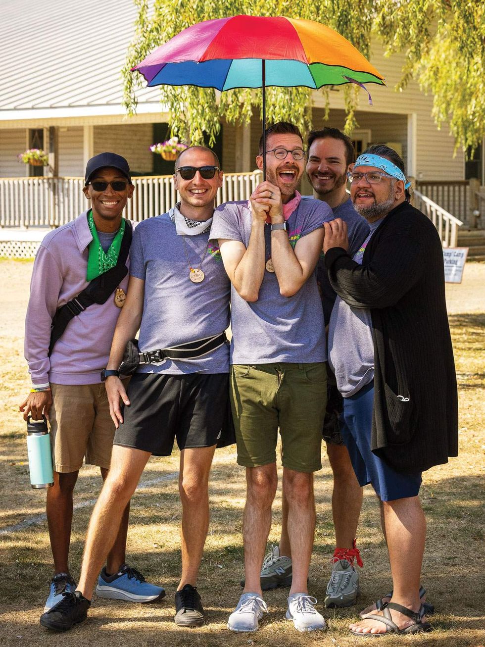 men pose under a rainbow umbrella at an adult lgbtq summer camp
