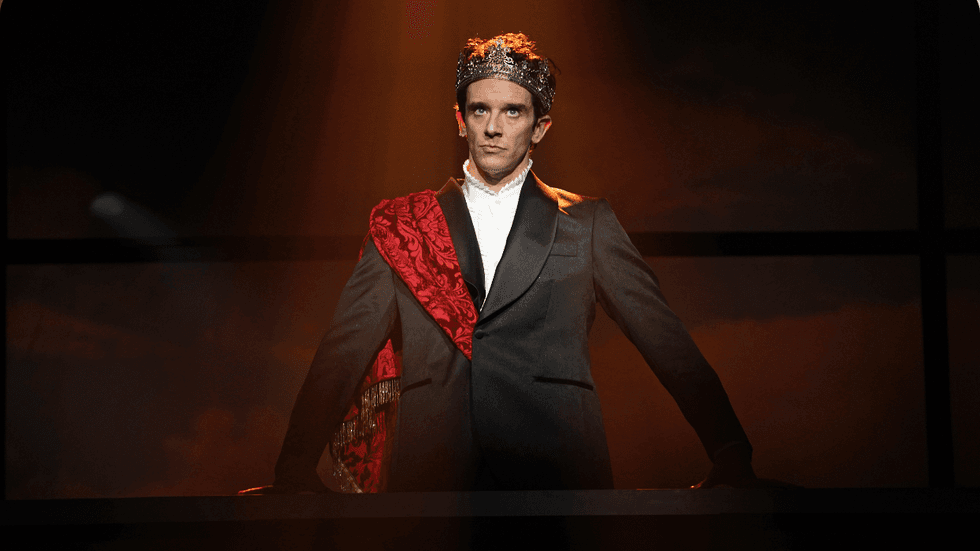 Michael Urie standing in a suit with a crown on his head