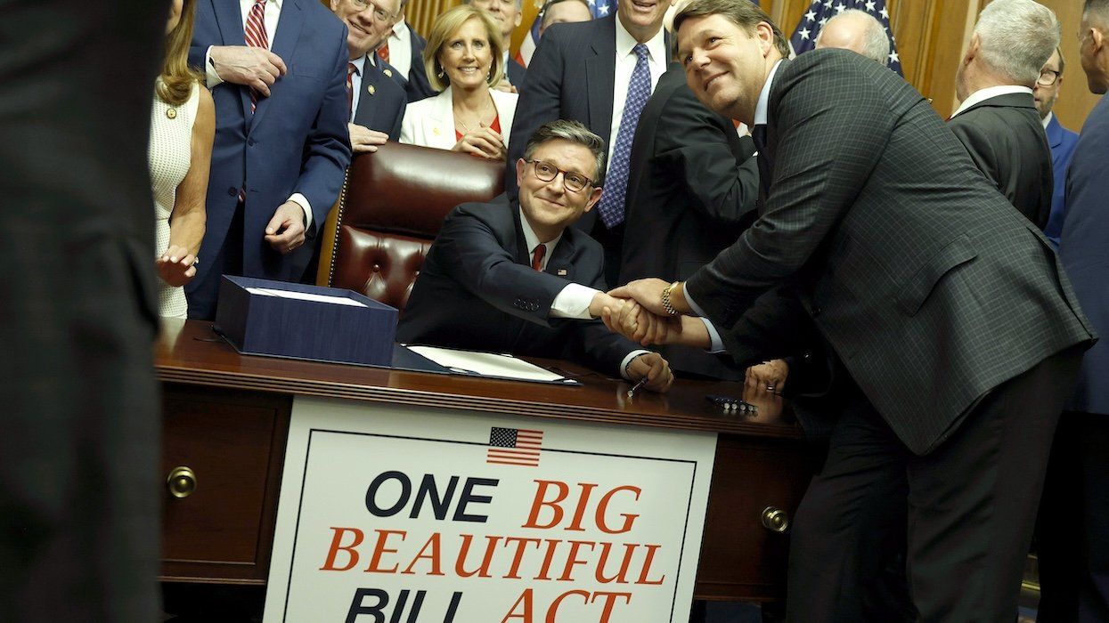 Mike Johnson sits at a desk with One Big Beautiful Act sign in front of it, shaking hands with a fellow Republican