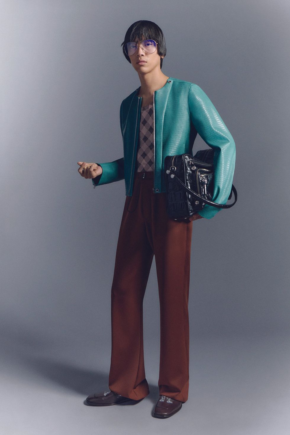 model wearing green jacket and brown slacks and a black bag