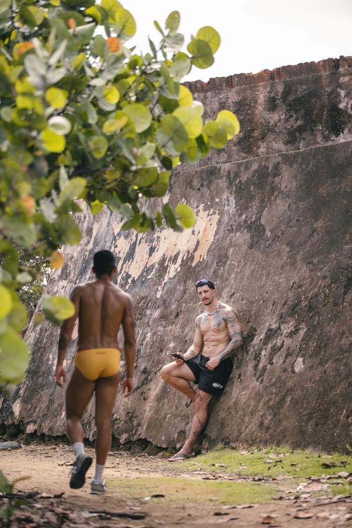 Models wearing Sniffies swimwear cross paths along a secluded coastal trail during the Sniffies Summer Swim Collection campaign in Puerto Rico