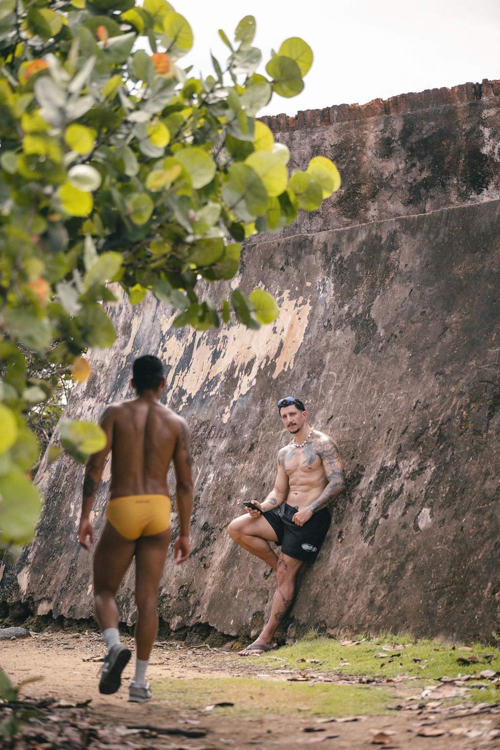 Models wearing Sniffies swimwear cross paths along a secluded coastal trail during the Sniffies Summer Swim Collection campaign in Puerto Rico