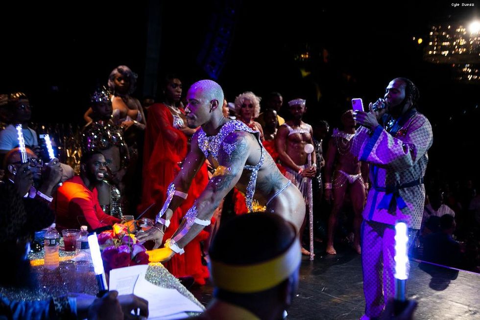 Mucular man in a thong bending over towards a judges panel.