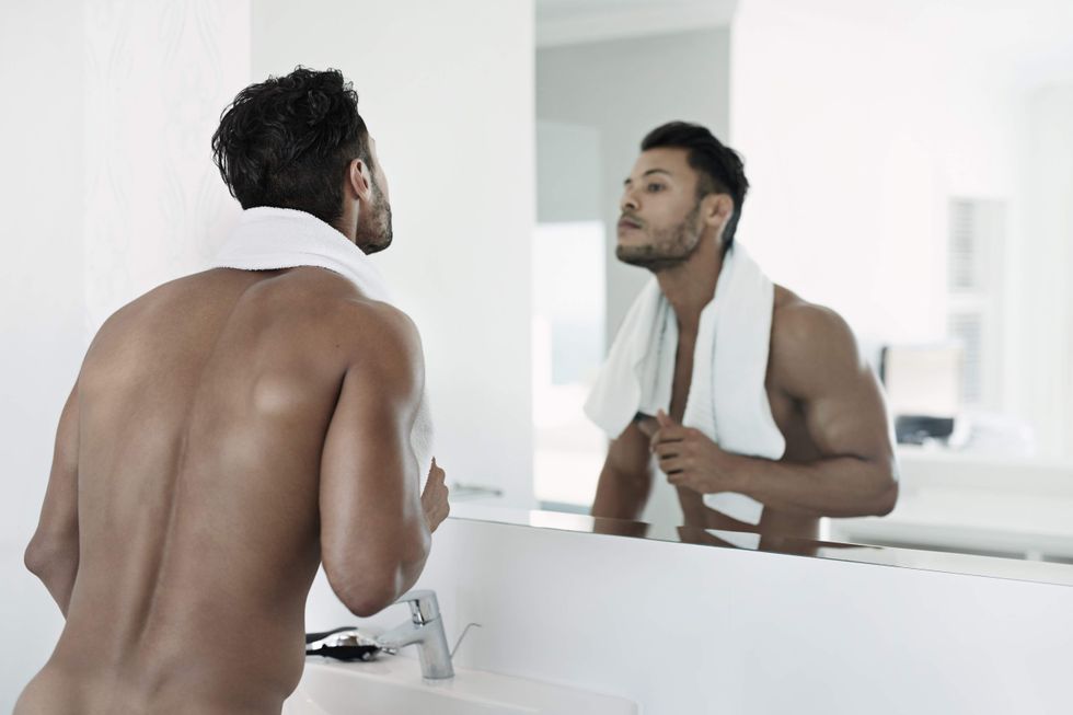 Naked man with a towel around his neck looking in a mirror