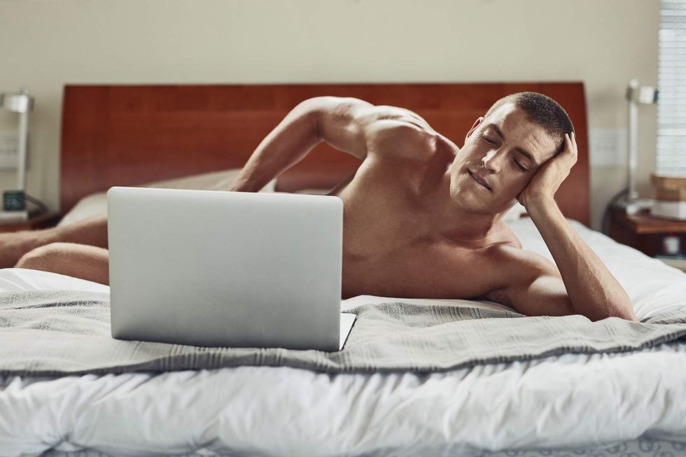 Nude man lying on his side with a laptop in front of him