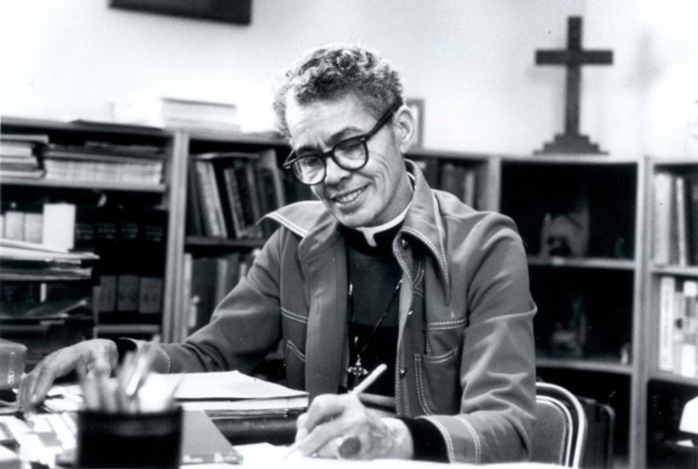 Pauli Murray in religious collar writing at a desk with bookshelves and a cross in the background from Carolina Digital Library and Archives