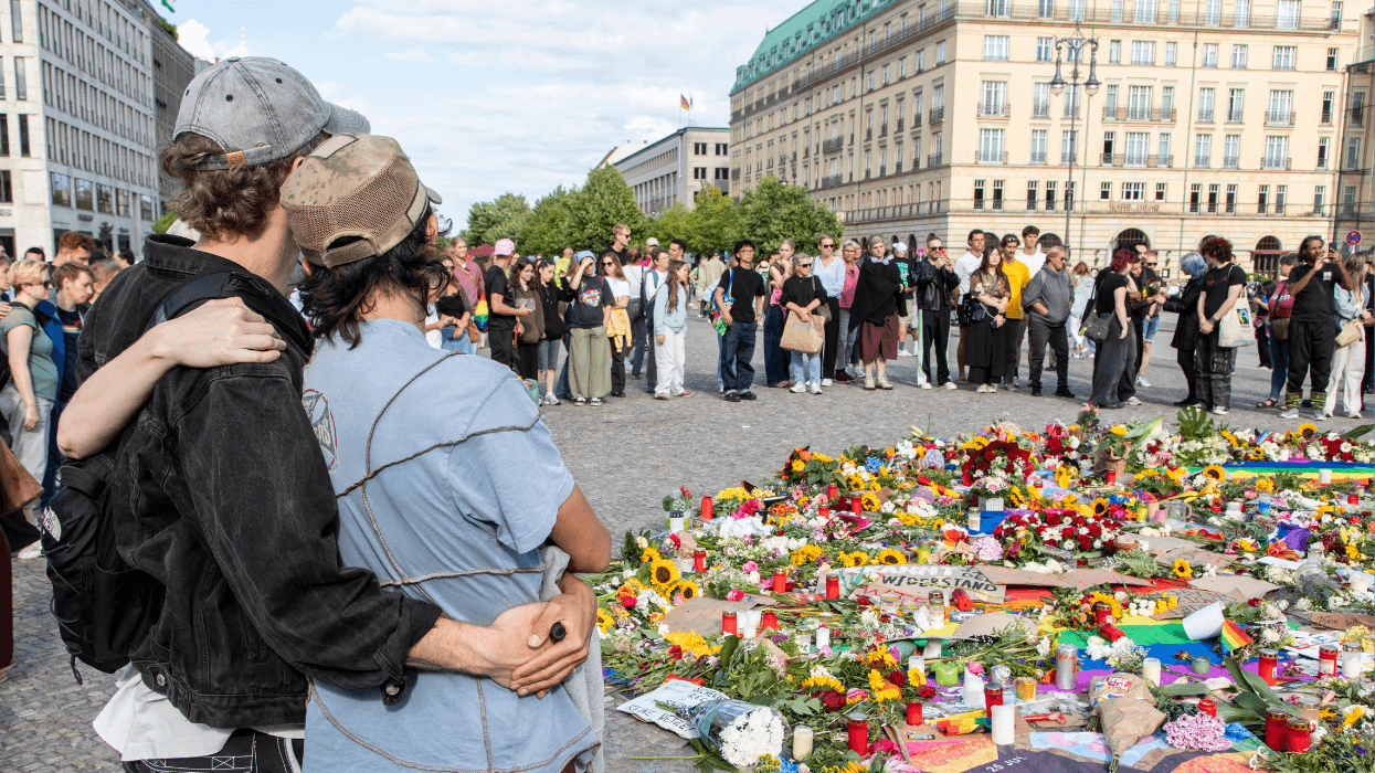 People stand beside a memorial of flowers and candles near Berlin's Brandenburg Gate after the Christopher Street Day attack.