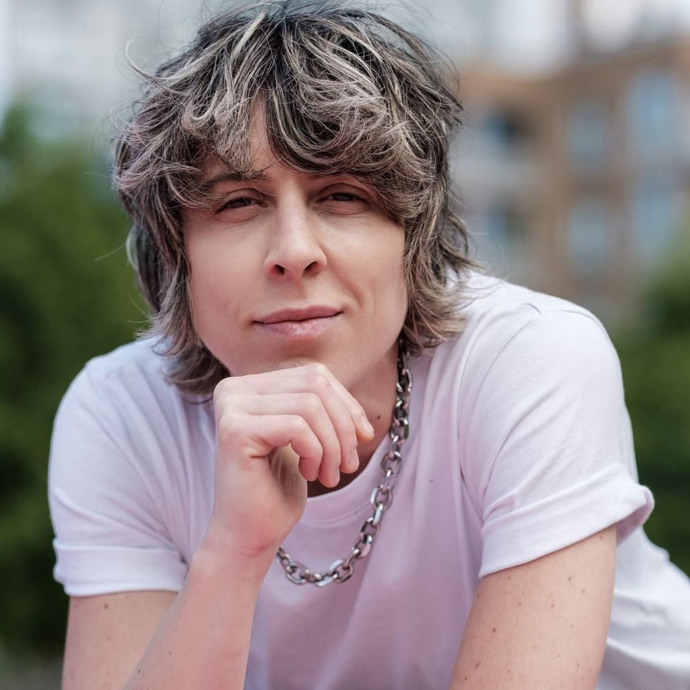 Person with gray hair looking into the camera with their chin resting on their hand