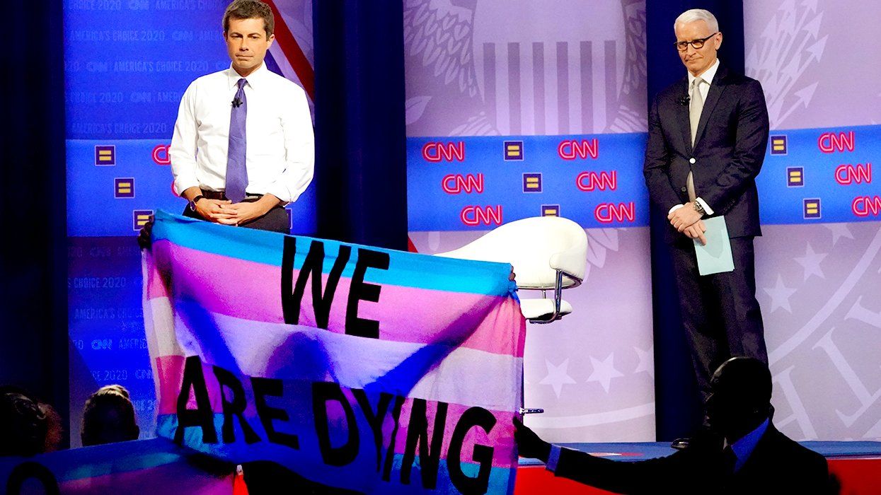 Pete Buttigieg and CNN moderator Anderson Cooper on stage while protester unveils Transgender flag says We Are Dying at Human Rights Campaign 2019 presidential town hall