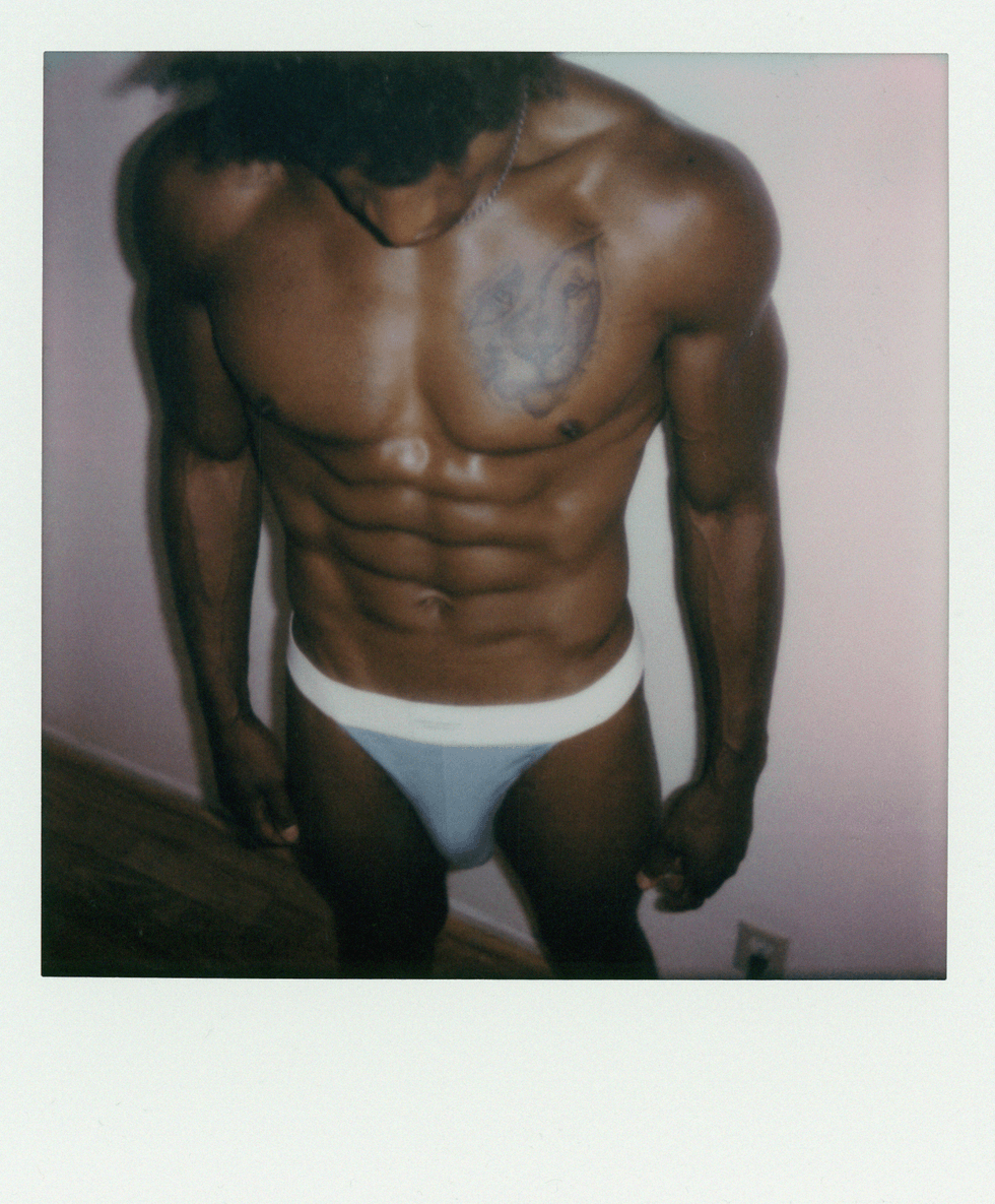 Polaroid close-up of a man\u2019s torso and abs wearing white briefs.
