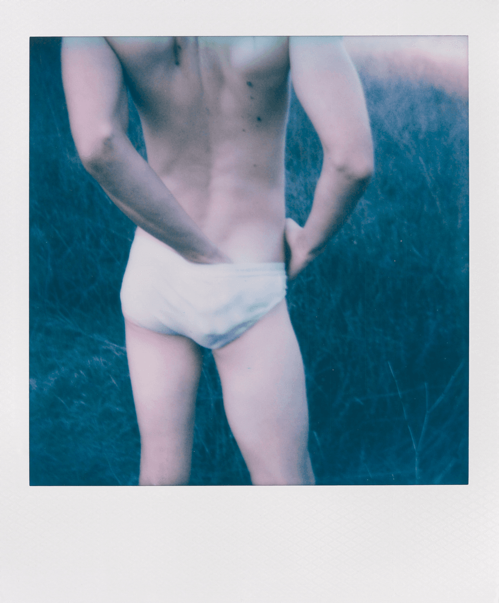 Polaroid close-up of a man\u2019s torso and legs wearing white briefs.