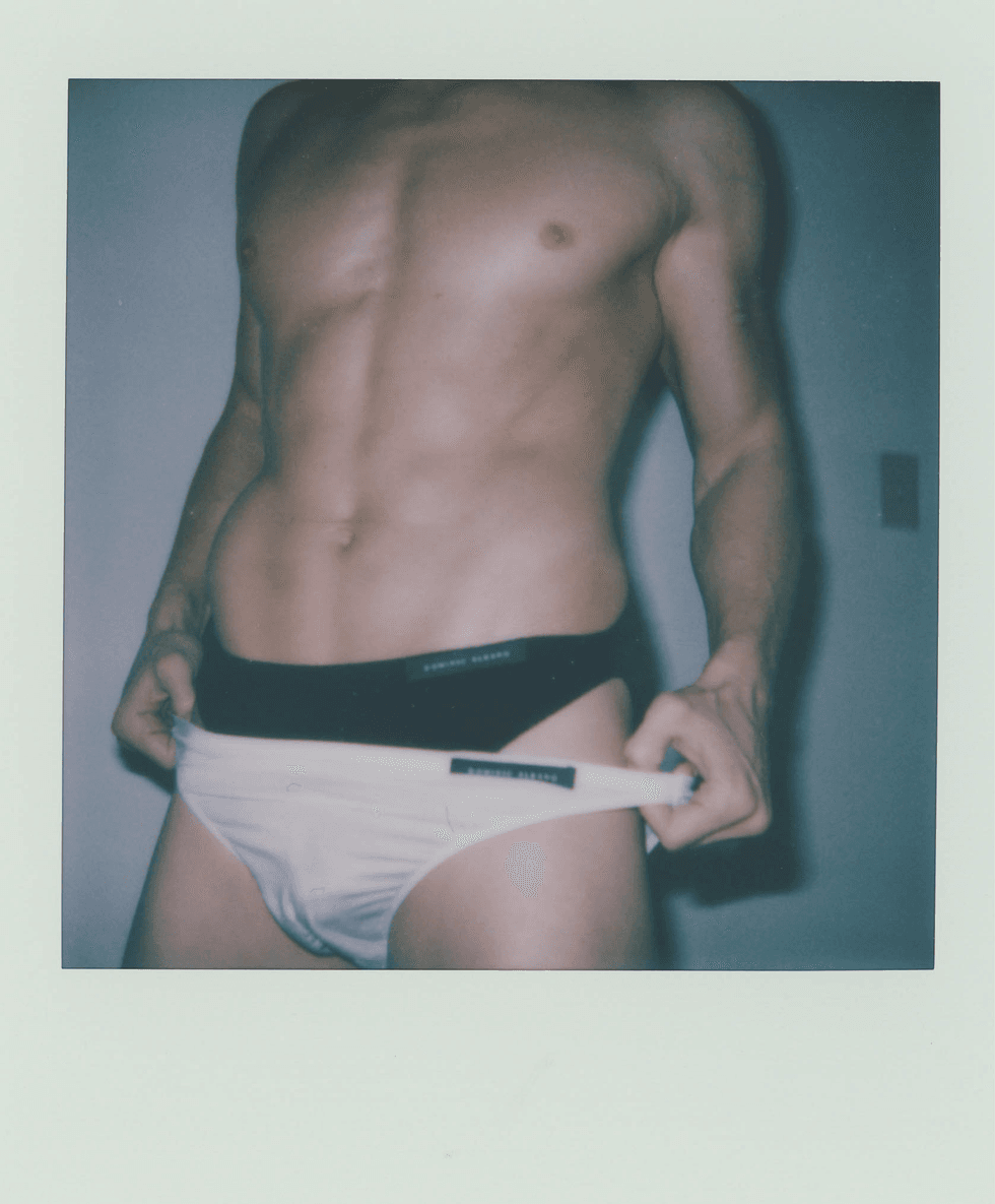 Polaroid portrait of a man adjusting his waistband while wearing briefs.