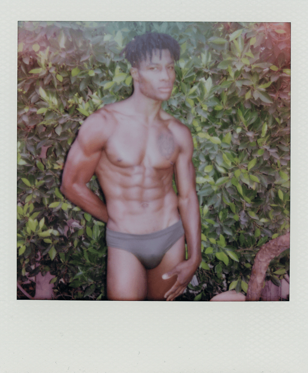 Polaroid portrait of a man standing outdoors in briefs in front of greenery.