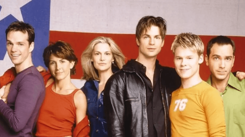 Promotional cast image from Queer as Folk featuring the ensemble in front of an American flag backdrop