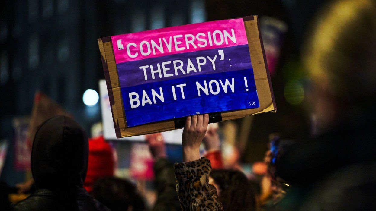 Protest with person holding placard that reads "conversion therapy: ban it now."