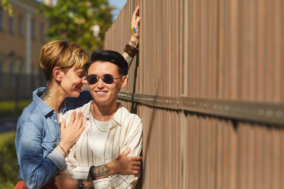 Queer couple leaning against a fence