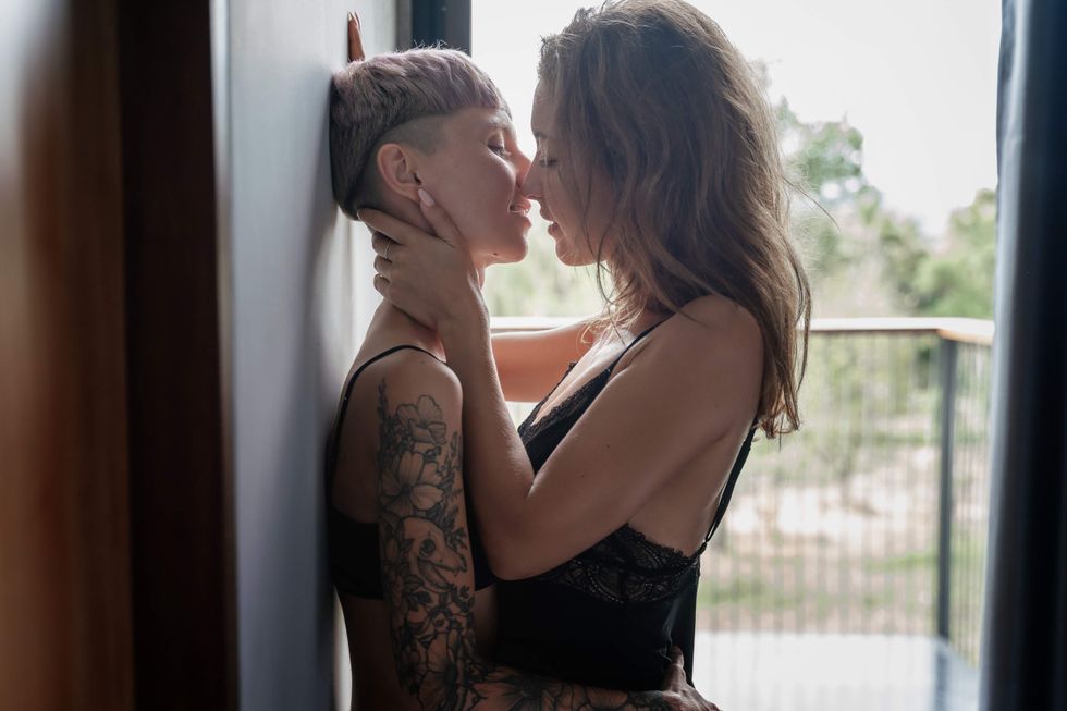Sapphic couple kissing against a wall