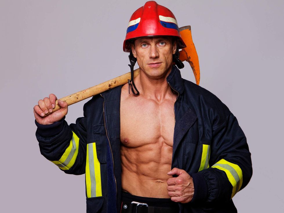 Shirtless man in a firefighter costume holding an ax