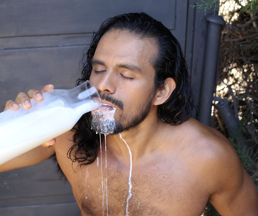 shirtless man outside drinking milk spills from glass bottle