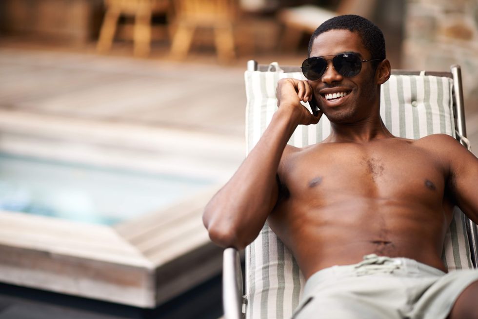 Shirtless man talking on his cell phone while sitting on a lounge chair