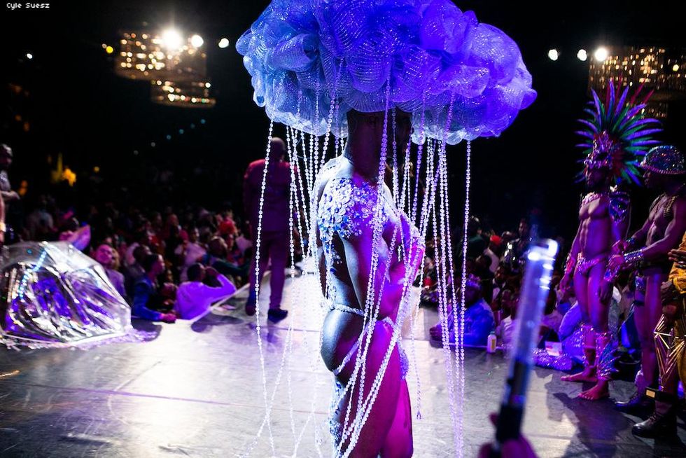 Shirtless muscular man in underwear with a headpiece that looks like a cloud that has crystals dripping from it to mock rain.