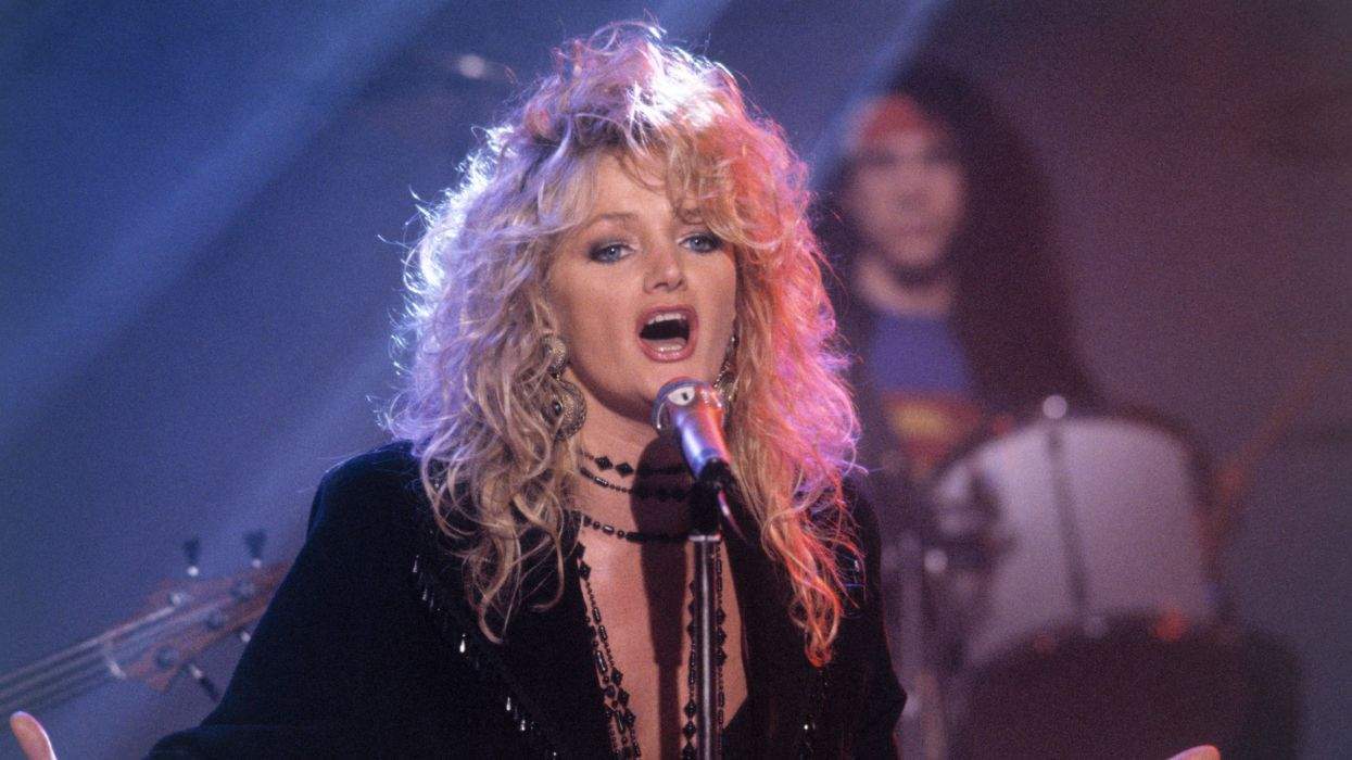 Singer with curly hair performing energetically on stage with a microphone.