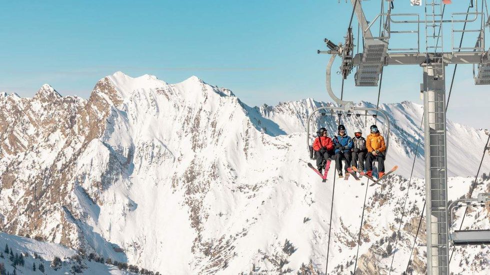 Skiers on a lift ride with snowy mountains in the background.
