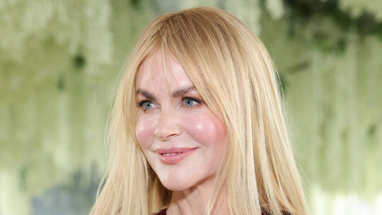 Smiling person in a red sequined dress with long blonde hair against a blurred leafy background.