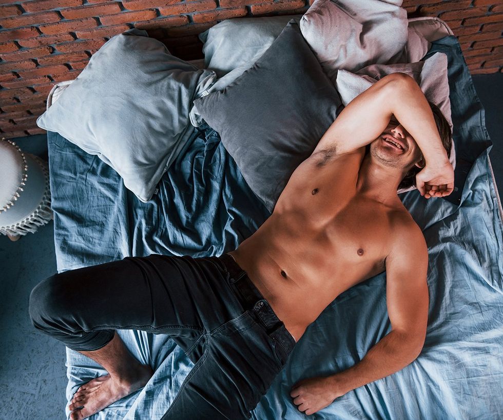 smiling shirtless man in bed with jeans and arm over face