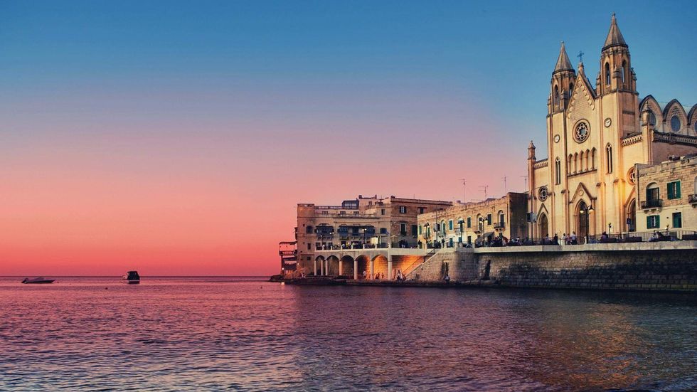 Sunset over Balluta Bay in Malta, where historic architecture lines the waterfront along the Mediterranean Sea