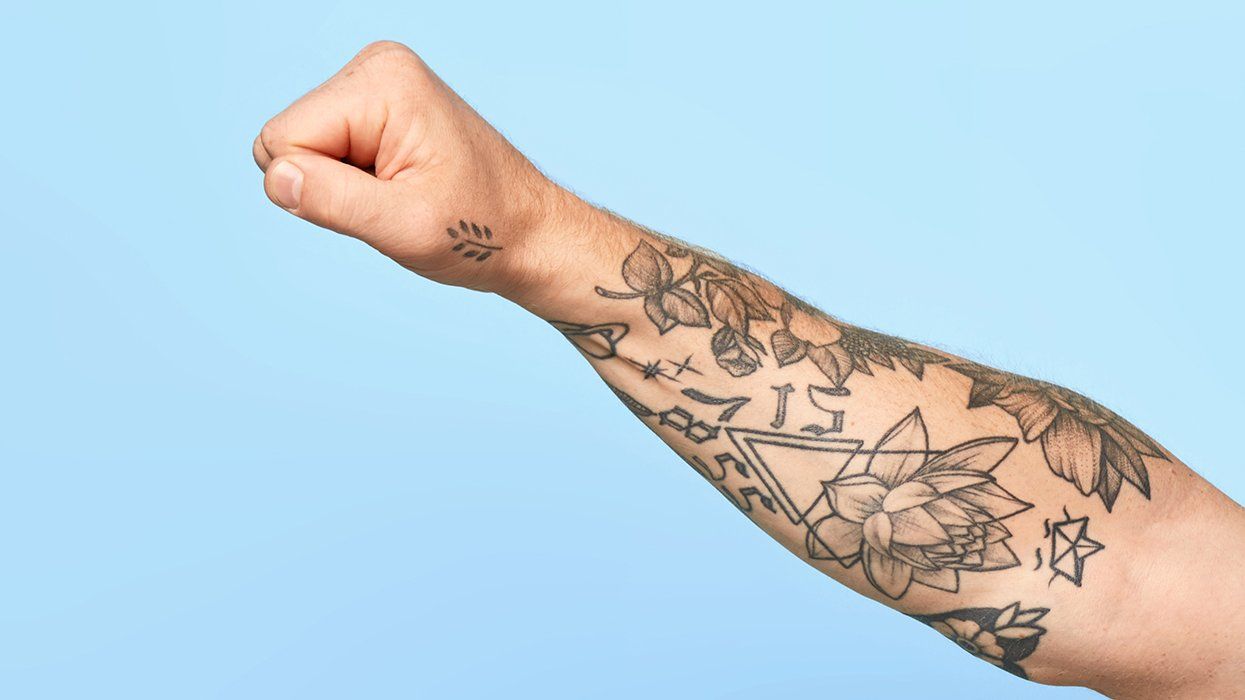tattooed arm making a fist against a blue background