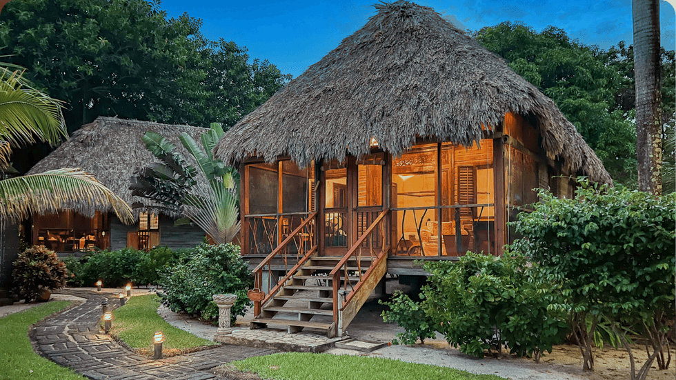 Thatched-roof cottage at Turtle Inn, featuring a screened veranda, wooden steps, and lush tropical landscaping.