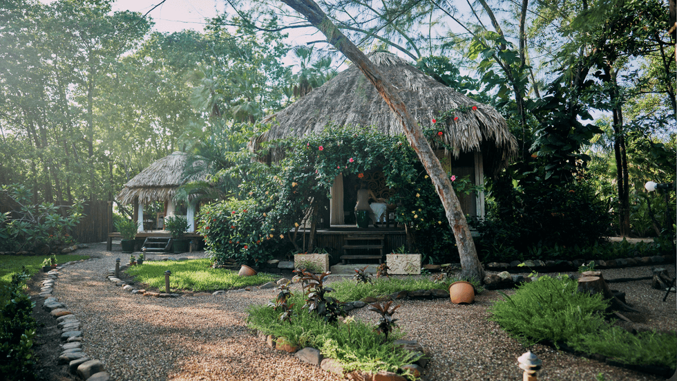 Thatched-roof spa cottage at Turtle Inn surrounded by lush tropical gardens and flowering vines.