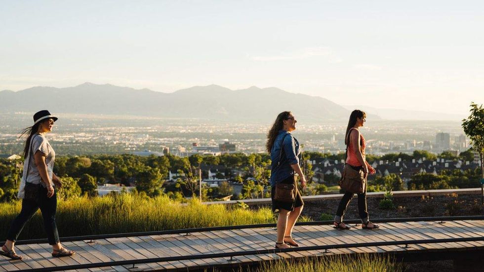 Three women walking on a boardwalk with city and mountains in the background.