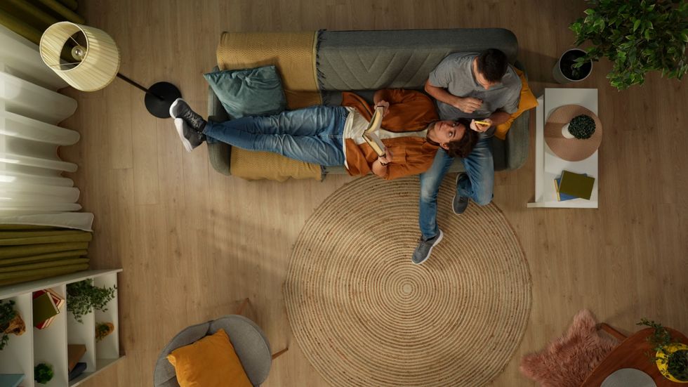 Top view capturing a homosexual male couple spending time together. One is reading a book, laying on the lap of the other man who is using his smartphone.