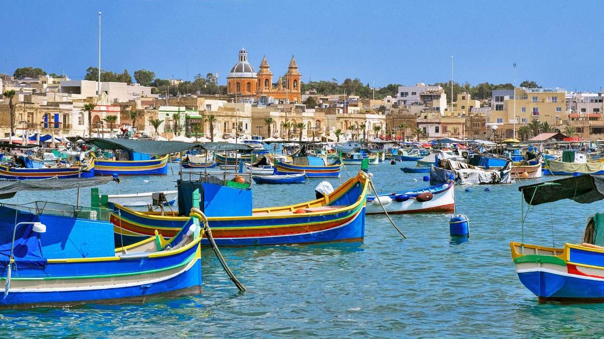 Traditional colorful fishing boats floating in the harbor of Marsaxlokk, Malta, with historic buildings and a church in the background