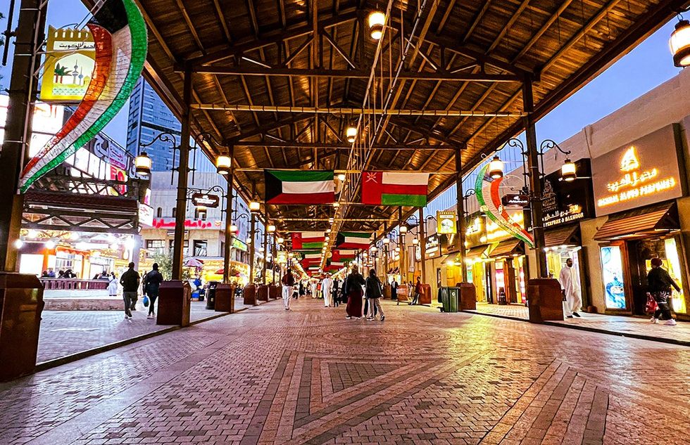 Traditional market Kuwait City many flags people walk along brick paved path surrounded by shops vibrant atmosphere