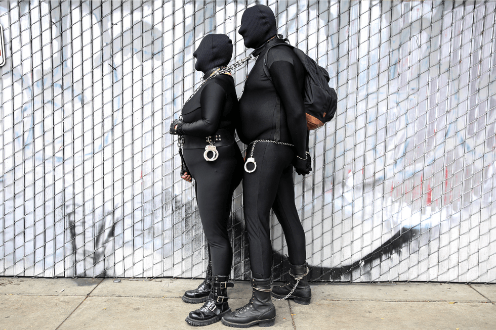 Two attendees dressed head-to-toe in black fetish gear pose during Folsom Street Fair weekend in San Francisco.