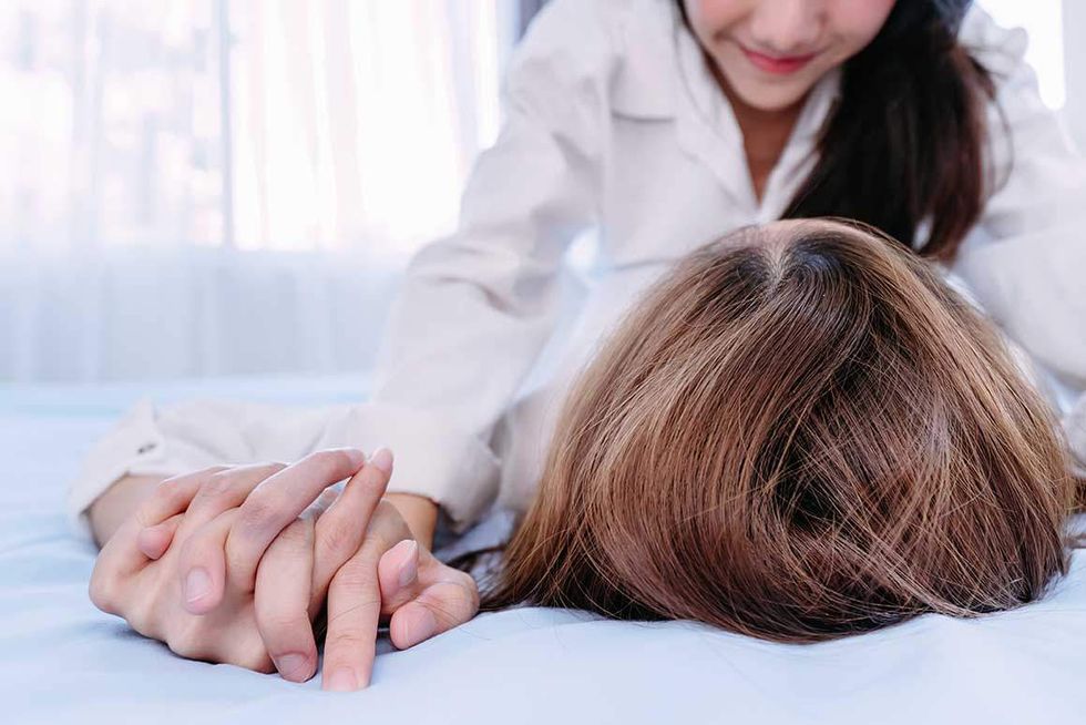 Two lesbians in bed, one on top of the other while they hold hands