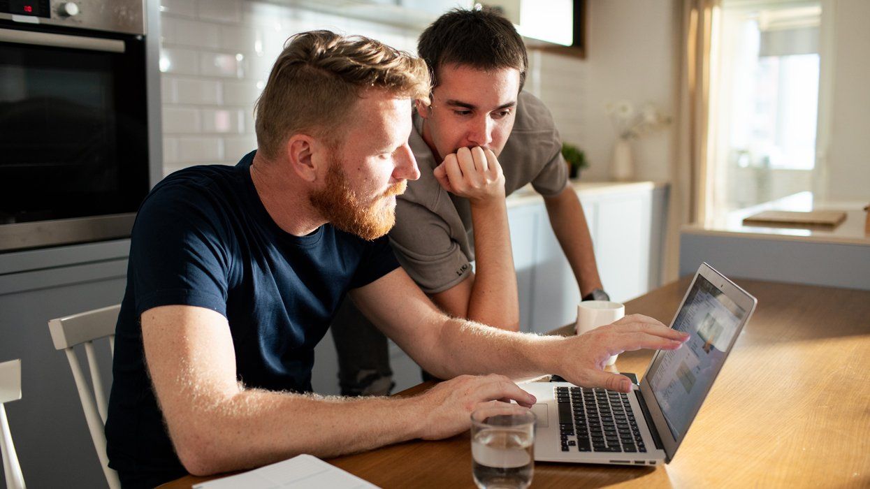 two men at a kitchen table looking at a laptop computer