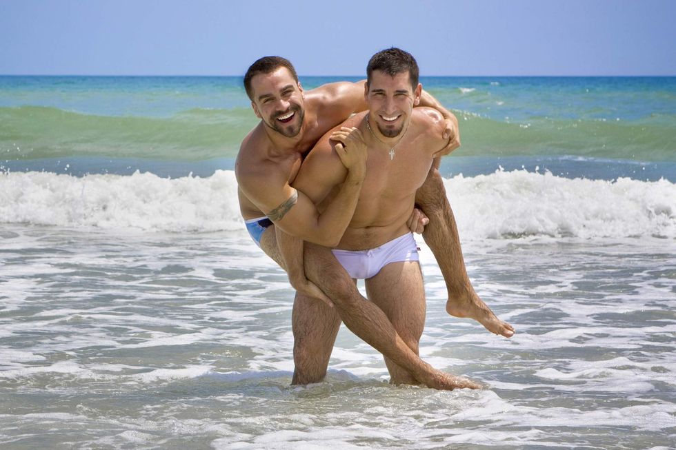 Two men in swim shorts, one carrying the other piggyback