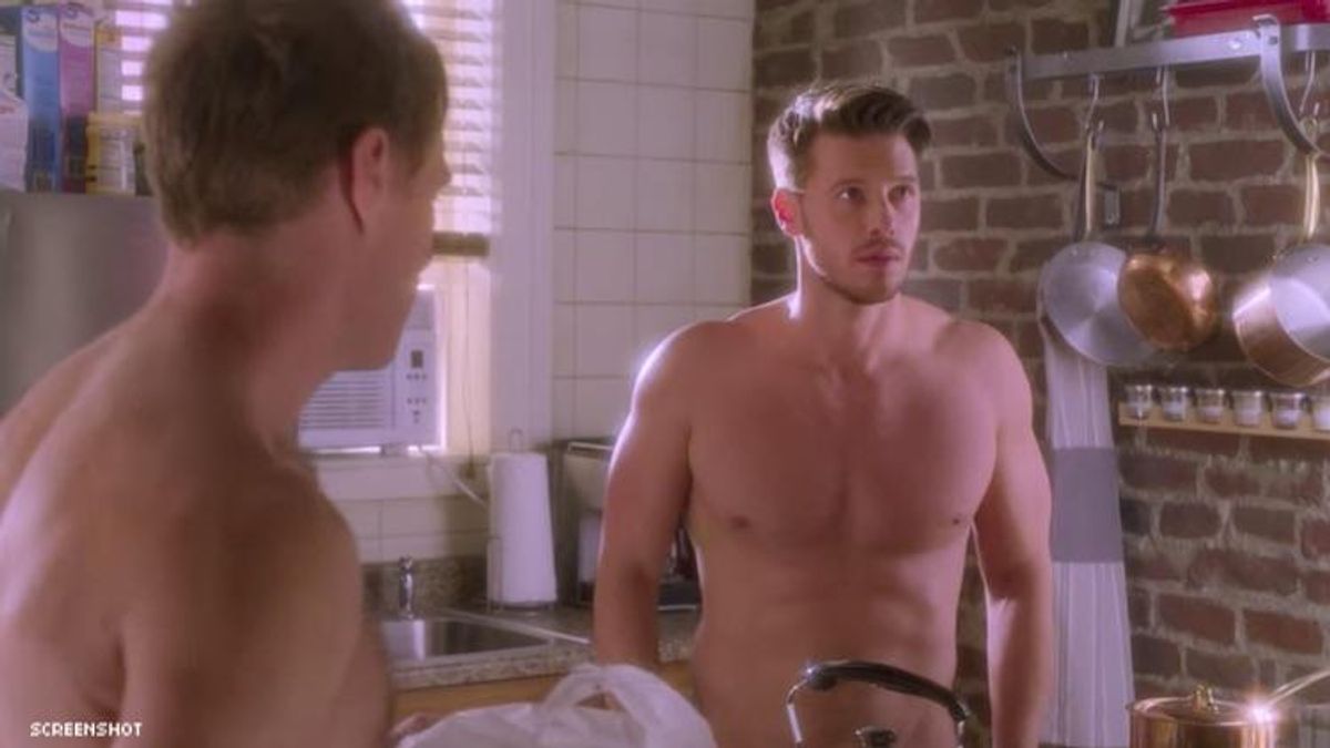 Two men standing in a kitchen with no shirts on.