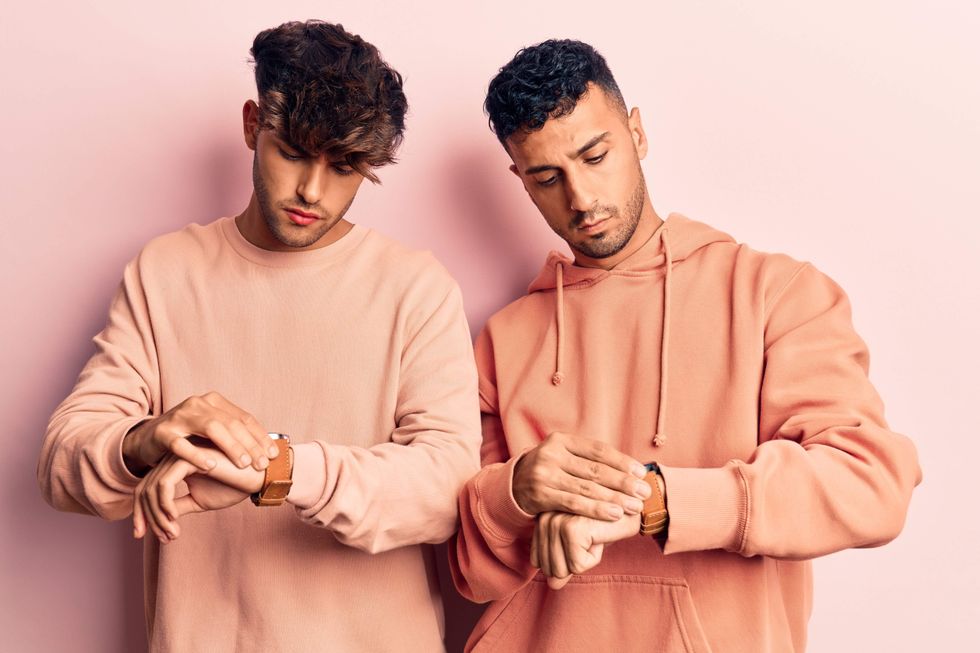 Two men wearing similar clothing, both looking at their watches